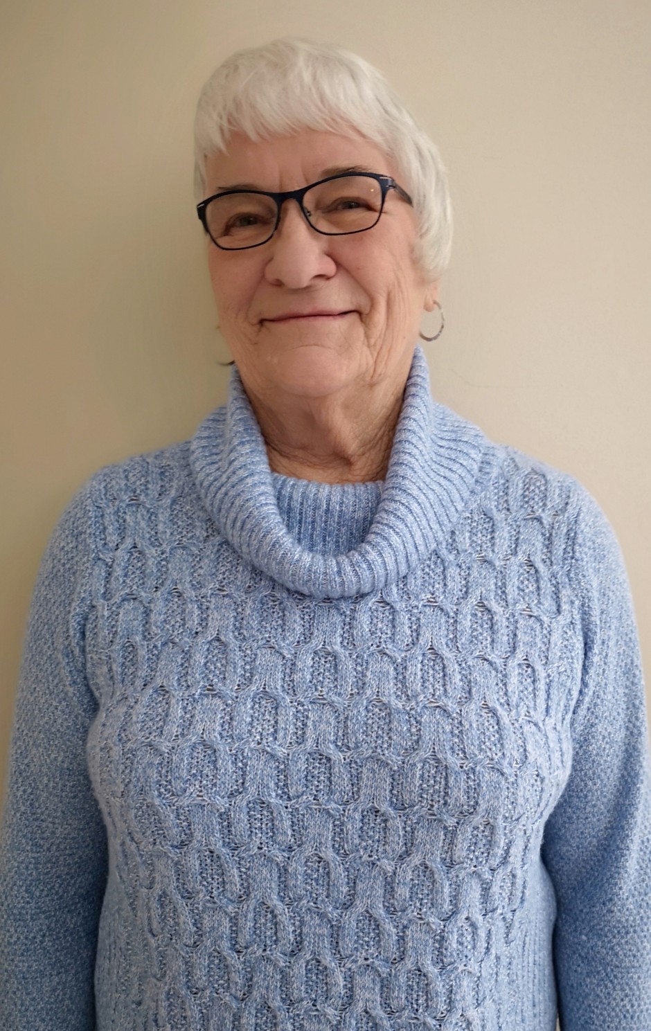 Elderly woman in light blue knit sweater wearing glasses, smiling